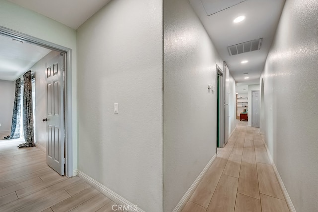 hall featuring visible vents, baseboards, wood finish floors, and a textured wall