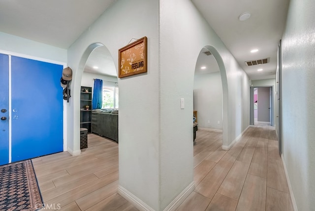 hall featuring baseboards, visible vents, arched walkways, and wood finish floors