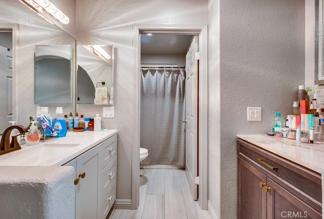 bathroom with vanity, a shower with curtain, wood finished floors, toilet, and a textured wall