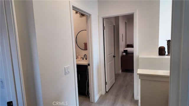 corridor with light wood-style flooring and a sink