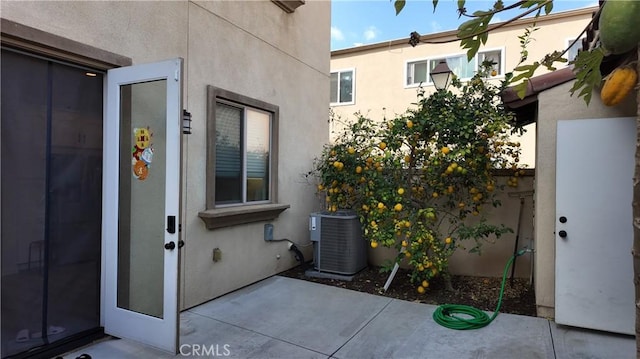 entrance to property featuring a patio area, central AC, and stucco siding