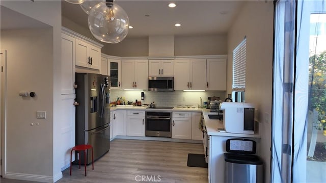 kitchen with light wood-type flooring, backsplash, recessed lighting, appliances with stainless steel finishes, and white cabinets