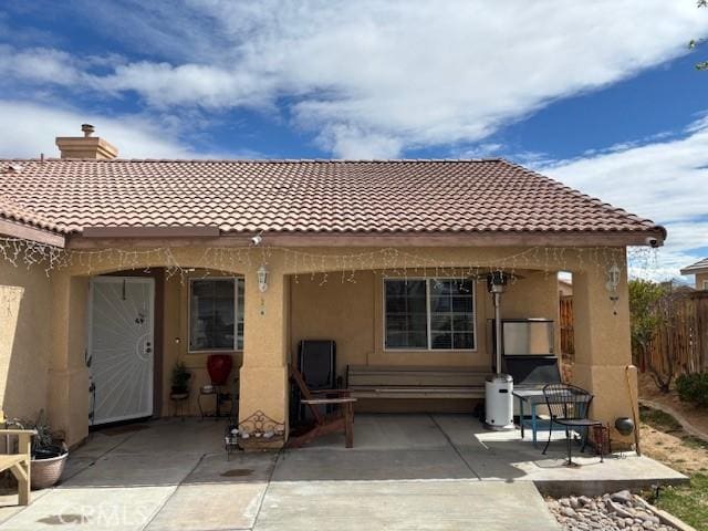 rear view of property with stucco siding, a patio, a chimney, and fence