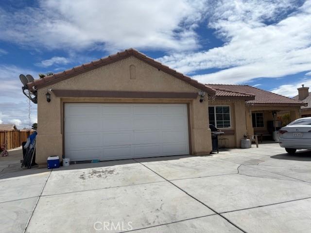 view of front of house with stucco siding, driveway, an attached garage, and fence