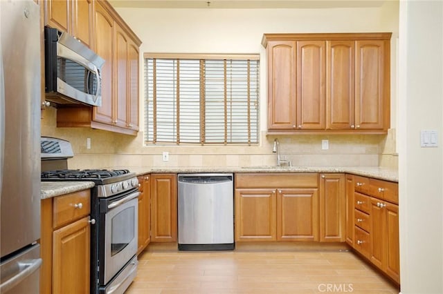 kitchen with light wood finished floors, appliances with stainless steel finishes, tasteful backsplash, and a sink