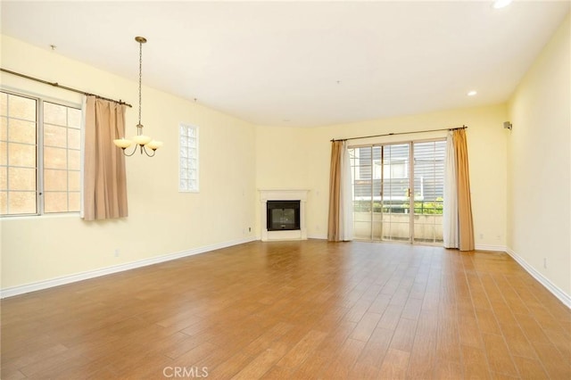 unfurnished living room with a glass covered fireplace, plenty of natural light, wood finished floors, and baseboards