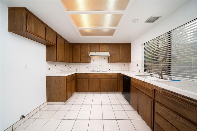 kitchen with under cabinet range hood, tile countertops, dishwasher, light tile patterned floors, and decorative backsplash