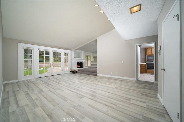 unfurnished living room featuring baseboards, vaulted ceiling, a warm lit fireplace, french doors, and light wood-style floors