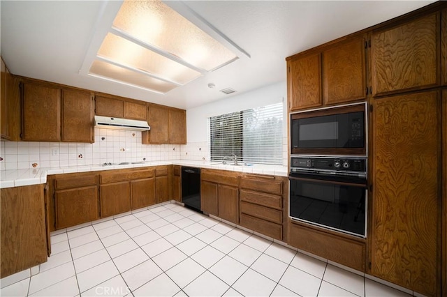 kitchen featuring black appliances, a sink, range hood, brown cabinetry, and tile counters