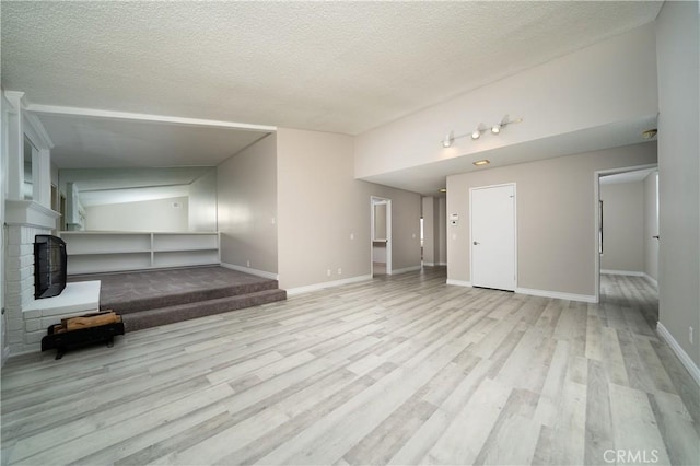 unfurnished living room with baseboards, a textured ceiling, wood finished floors, and a fireplace