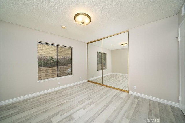 unfurnished bedroom featuring baseboards, wood finished floors, a closet, and a textured ceiling