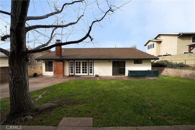 rear view of property with fence, a tiled roof, a lawn, a chimney, and a patio