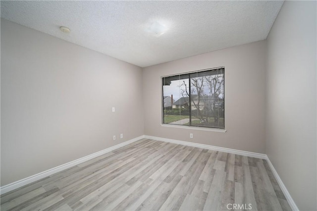 empty room featuring baseboards, light wood-type flooring, and a textured ceiling