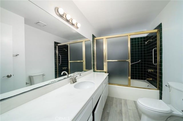 full bath featuring vanity, wood finished floors, visible vents, toilet, and combined bath / shower with glass door