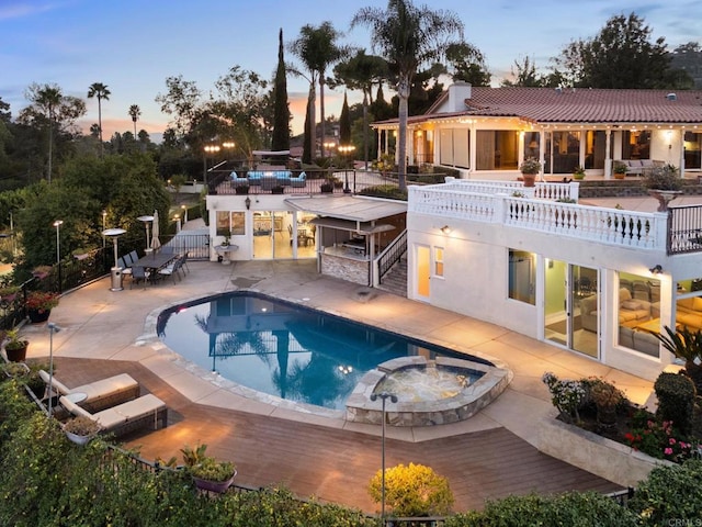 pool at dusk with a pool with connected hot tub, a patio, and fence