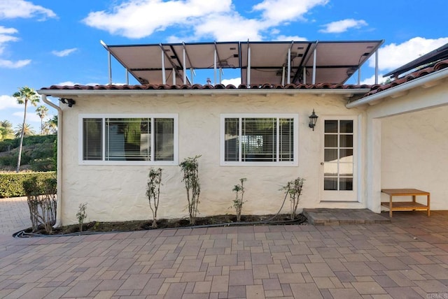 rear view of property with a tile roof, a patio area, and stucco siding