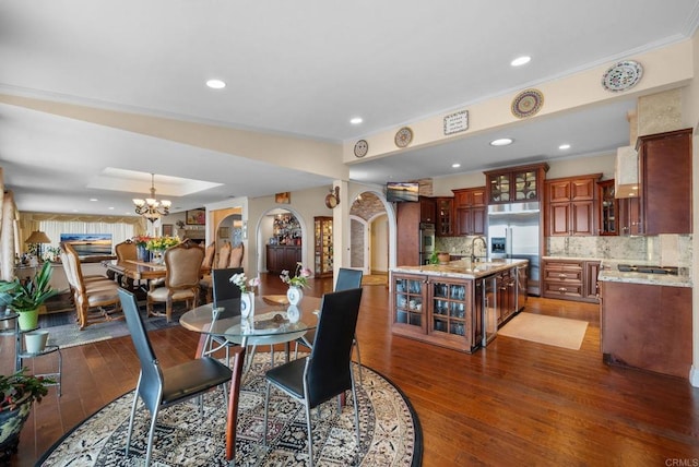 dining space with arched walkways, ornamental molding, an inviting chandelier, and hardwood / wood-style floors