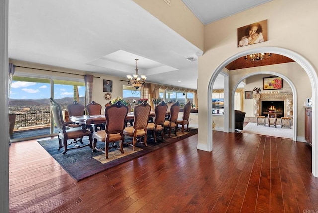 dining area featuring visible vents, an inviting chandelier, a tray ceiling, a lit fireplace, and hardwood / wood-style flooring