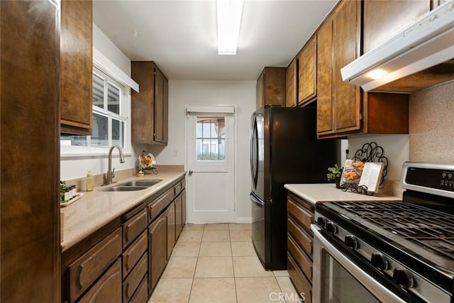 kitchen with stainless steel gas range oven, under cabinet range hood, light countertops, light tile patterned floors, and a sink