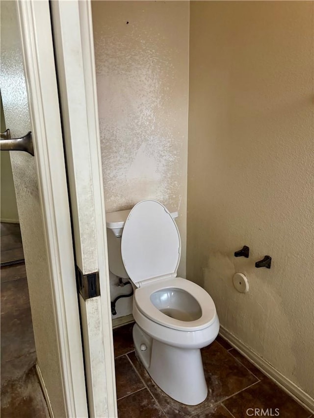 bathroom with a textured wall, toilet, and tile patterned flooring