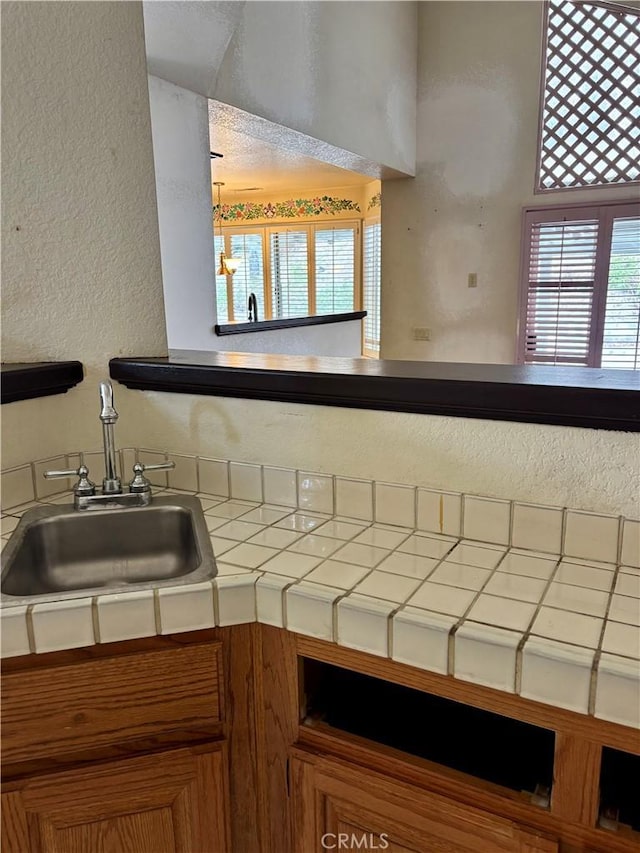 kitchen with a sink, a healthy amount of sunlight, a textured wall, and tile counters