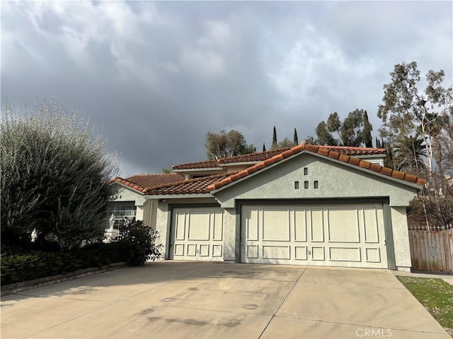 mediterranean / spanish-style house featuring stucco siding, a tile roof, fence, concrete driveway, and an attached garage