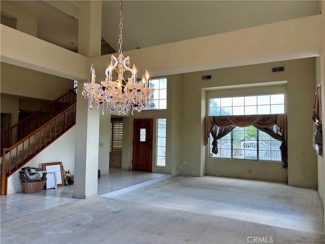 carpeted foyer featuring visible vents, stairs, a towering ceiling, tile patterned floors, and a chandelier