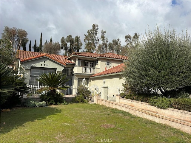 mediterranean / spanish-style home with a balcony, fence, stucco siding, a front lawn, and a garage