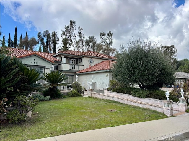 mediterranean / spanish-style house featuring a tile roof, stucco siding, a front yard, and a balcony