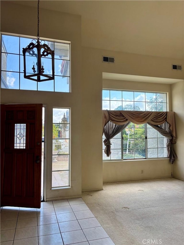 carpeted entrance foyer with visible vents, a high ceiling, an inviting chandelier, and tile patterned flooring