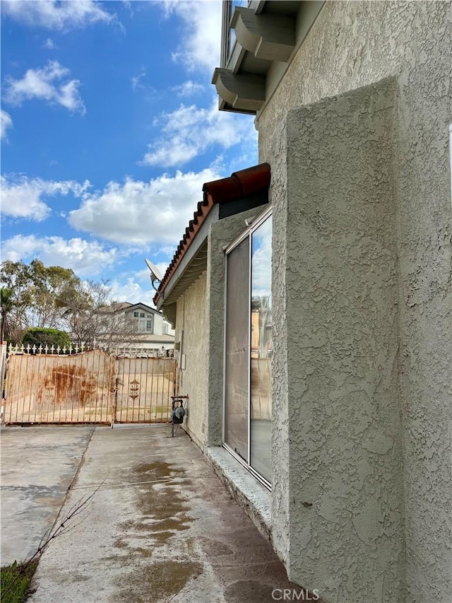 view of side of home with stucco siding, fence, and a gate