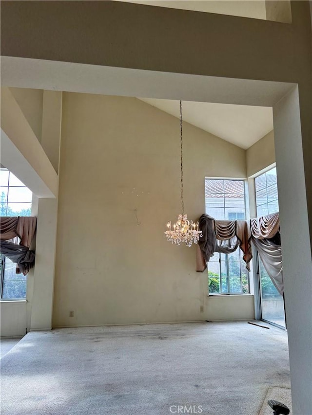 unfurnished dining area featuring a chandelier, high vaulted ceiling, and carpet floors