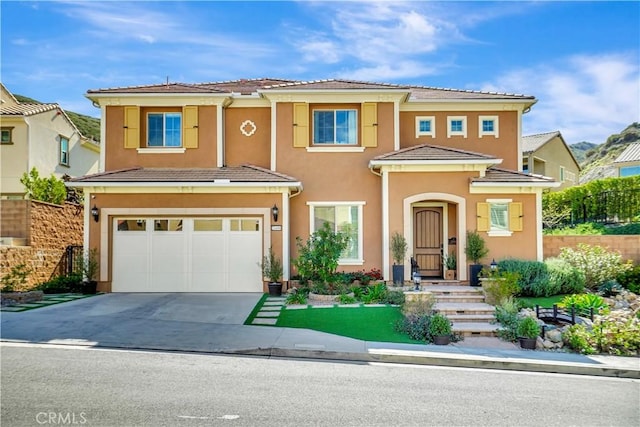 view of front of property with fence, a tile roof, concrete driveway, stucco siding, and a garage