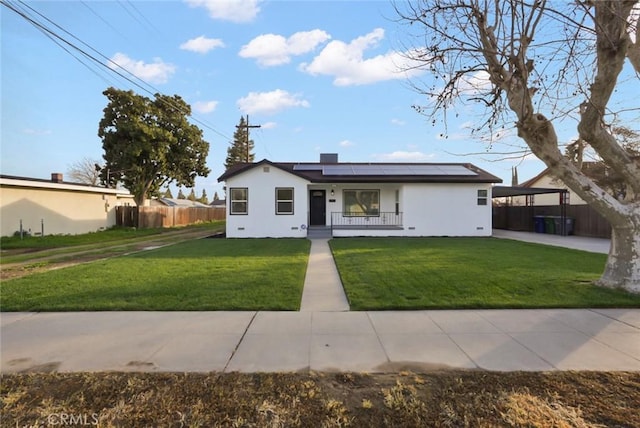 ranch-style home with a porch, fence, a front yard, and roof mounted solar panels