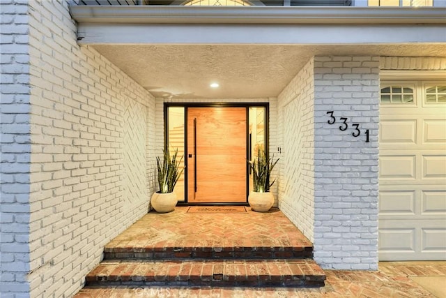 entrance to property featuring a garage and brick siding