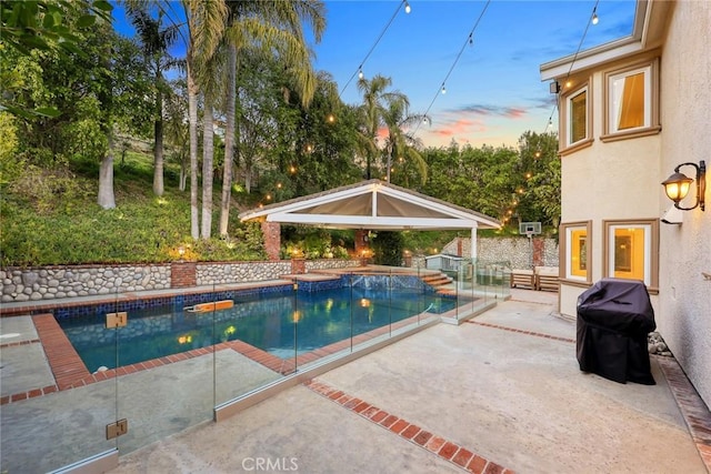 pool at dusk with a patio, fence, an outdoor pool, a gazebo, and grilling area