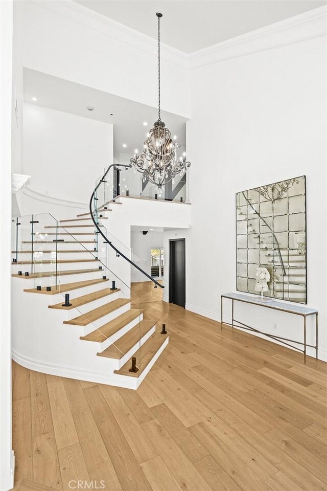 stairs with a notable chandelier, ornamental molding, wood-type flooring, baseboards, and a towering ceiling