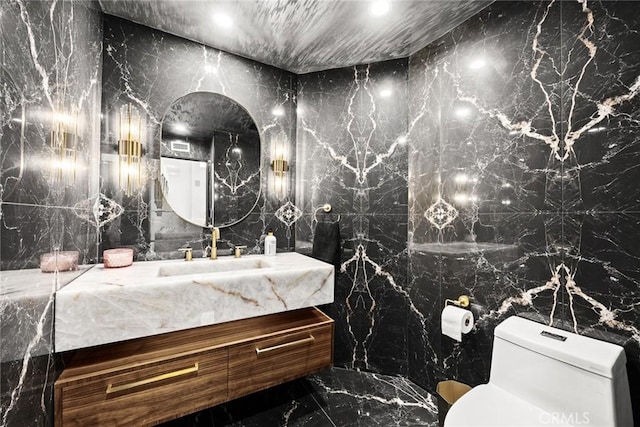 half bathroom featuring stone wall, toilet, marble finish floor, and vanity