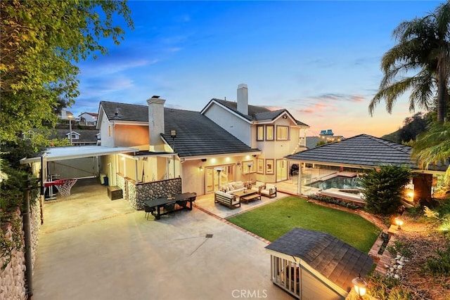 back of house at dusk featuring a patio, a yard, stucco siding, a chimney, and outdoor lounge area