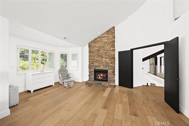 unfurnished living room featuring light wood-type flooring, visible vents, high vaulted ceiling, and a stone fireplace