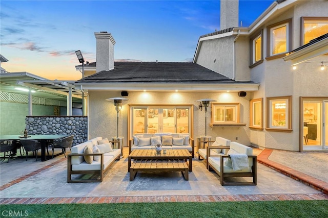 back of property at dusk featuring an outdoor living space, stucco siding, and a chimney