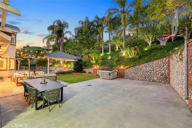 patio terrace at dusk with outdoor dining space, a lawn, an outdoor structure, and fence