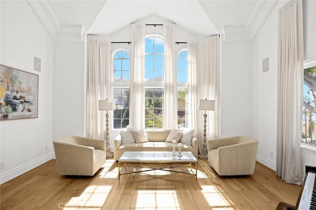 sitting room with vaulted ceiling, wood finished floors, baseboards, and ornamental molding