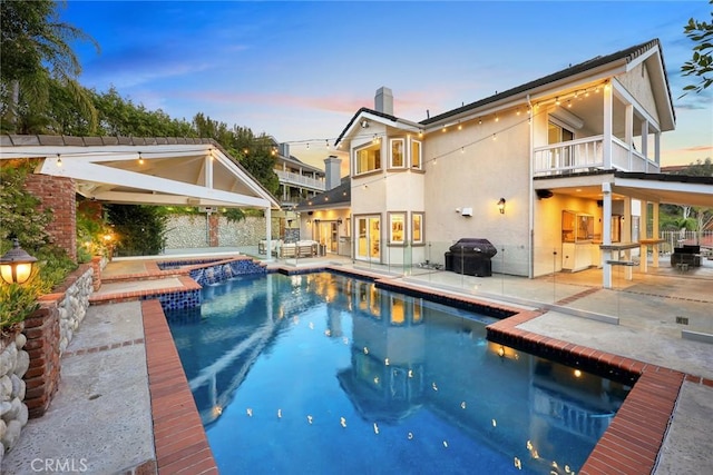 pool at dusk featuring a patio area, area for grilling, an outdoor pool, and an in ground hot tub