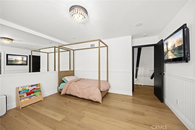 bedroom with a chandelier, a wainscoted wall, visible vents, and light wood-style floors