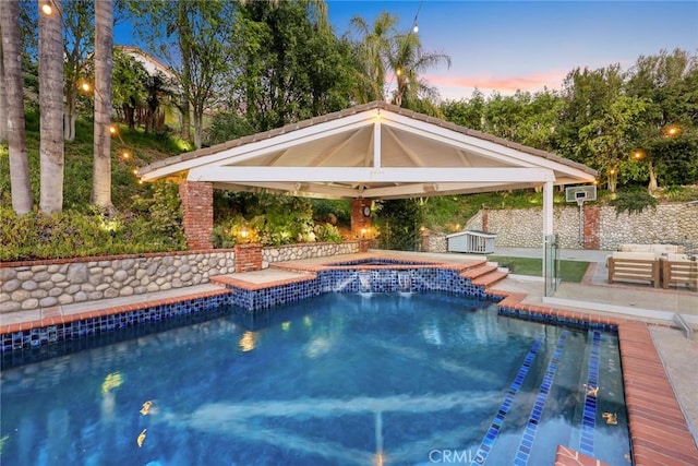 pool at dusk featuring a gazebo, a patio area, and a pool with connected hot tub