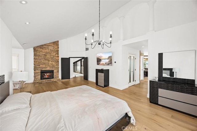 bedroom with baseboards, light wood-style flooring, a fireplace, an inviting chandelier, and high vaulted ceiling