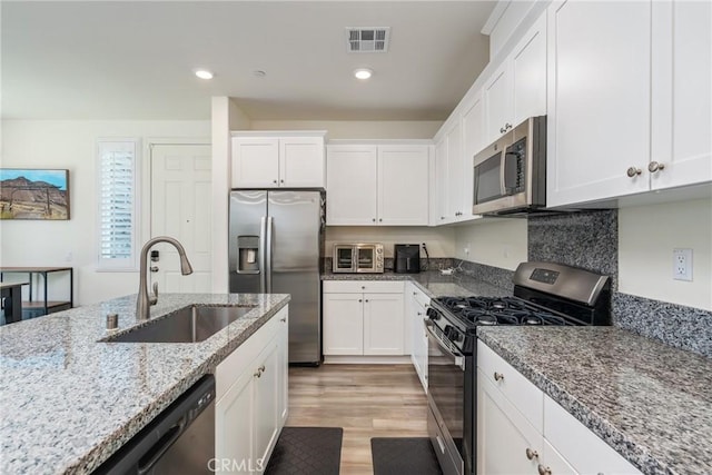 kitchen with visible vents, a sink, white cabinetry, stainless steel appliances, and light wood finished floors