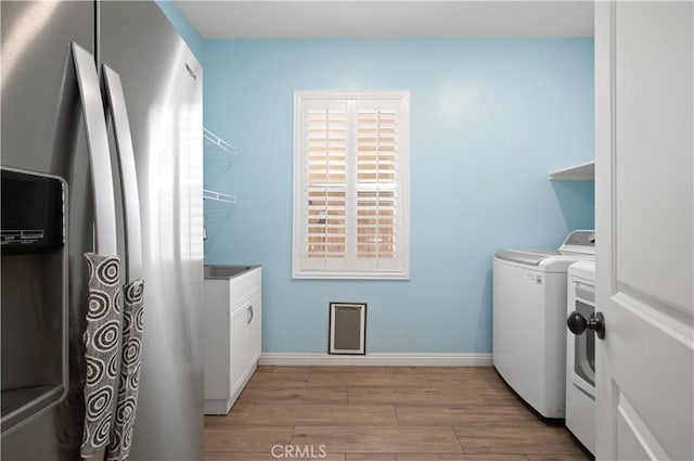 laundry area with cabinet space, separate washer and dryer, light wood-style floors, and baseboards