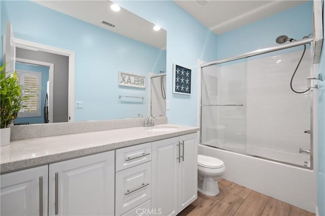 bathroom with vanity, wood finished floors, visible vents, bath / shower combo with glass door, and toilet